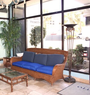 A wicker sofa with blue cushions, a glass coffee table, and a tall floor lamp.
