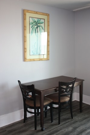 A dining area with a wooden table and two chairs, a framed botanical print on the wall, and a light-colored floor.