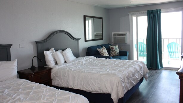 A hotel room with a large bed, a smaller bed, a nightstand, a dresser, a mirror, an air conditioning unit, and a view of the outside.