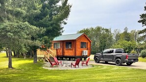 Une cabane avec une terrasse, des sièges d’extérieur et un camion garé à proximité.