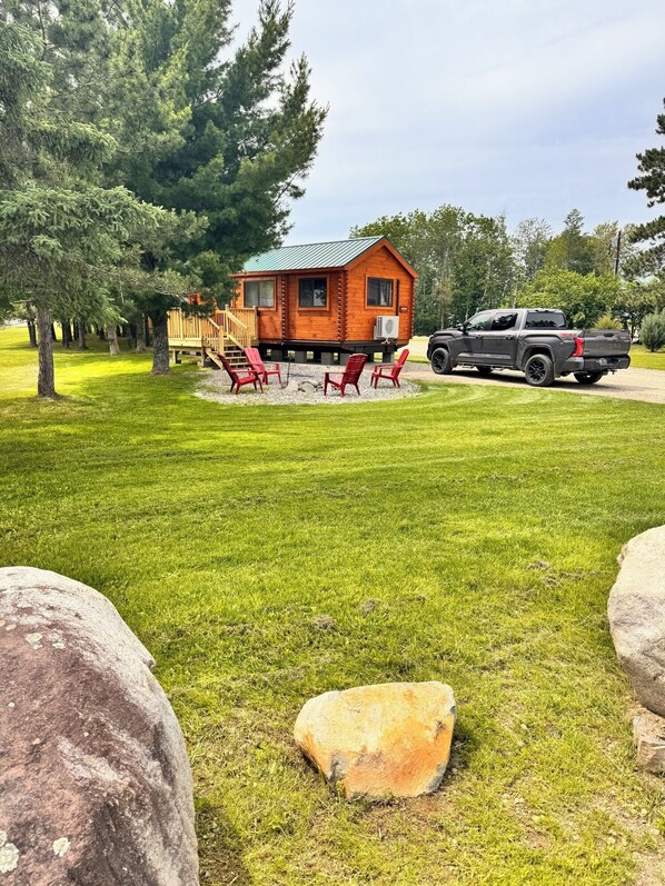 A cabin with a deck, outdoor seating, and a truck parked nearby.