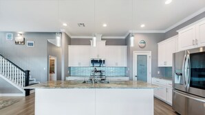 Une cuisine moderne avec des meubles blancs, un grand îlot central, des appareils en acier inoxydable et un plancher en bois.