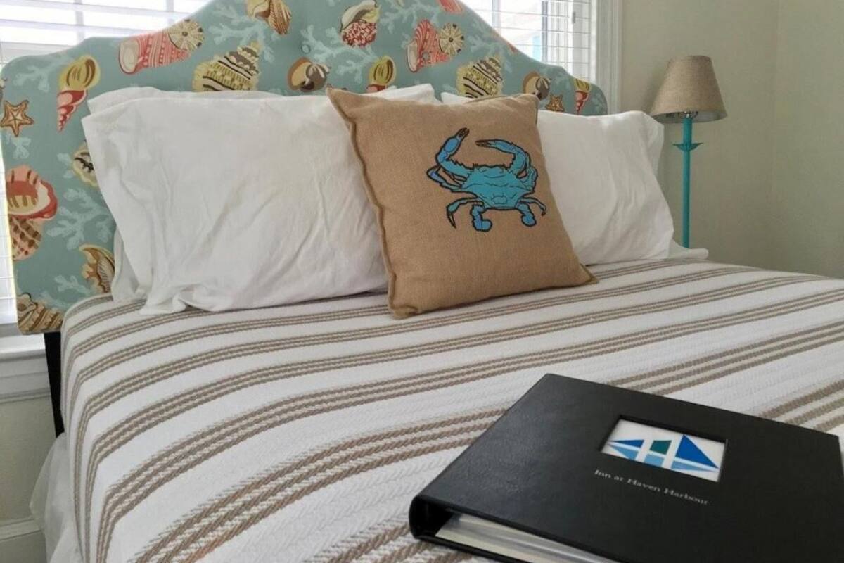 Una cama con ropa de cama a rayas, un cojín con diseño de cangrejo y un libro sobre la cama.