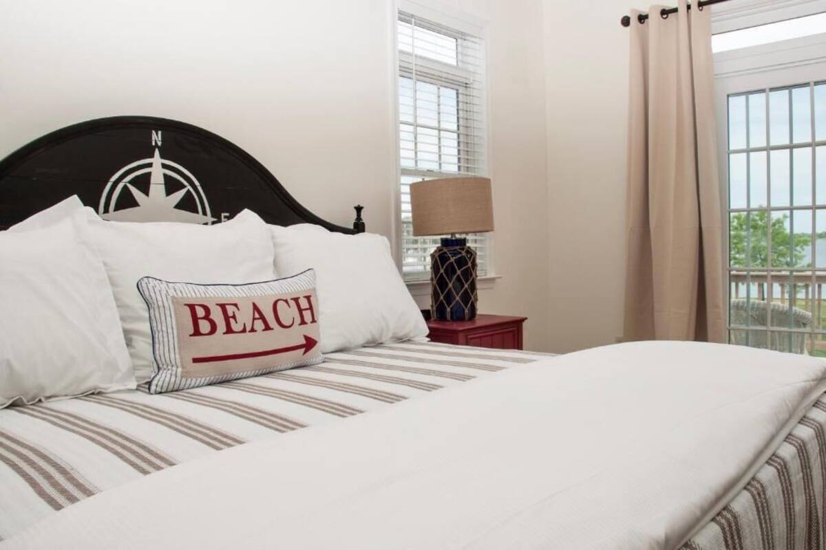 Una cama bien hecha con ropa de cama a rayas y una almohada con el texto 'BEACH'.