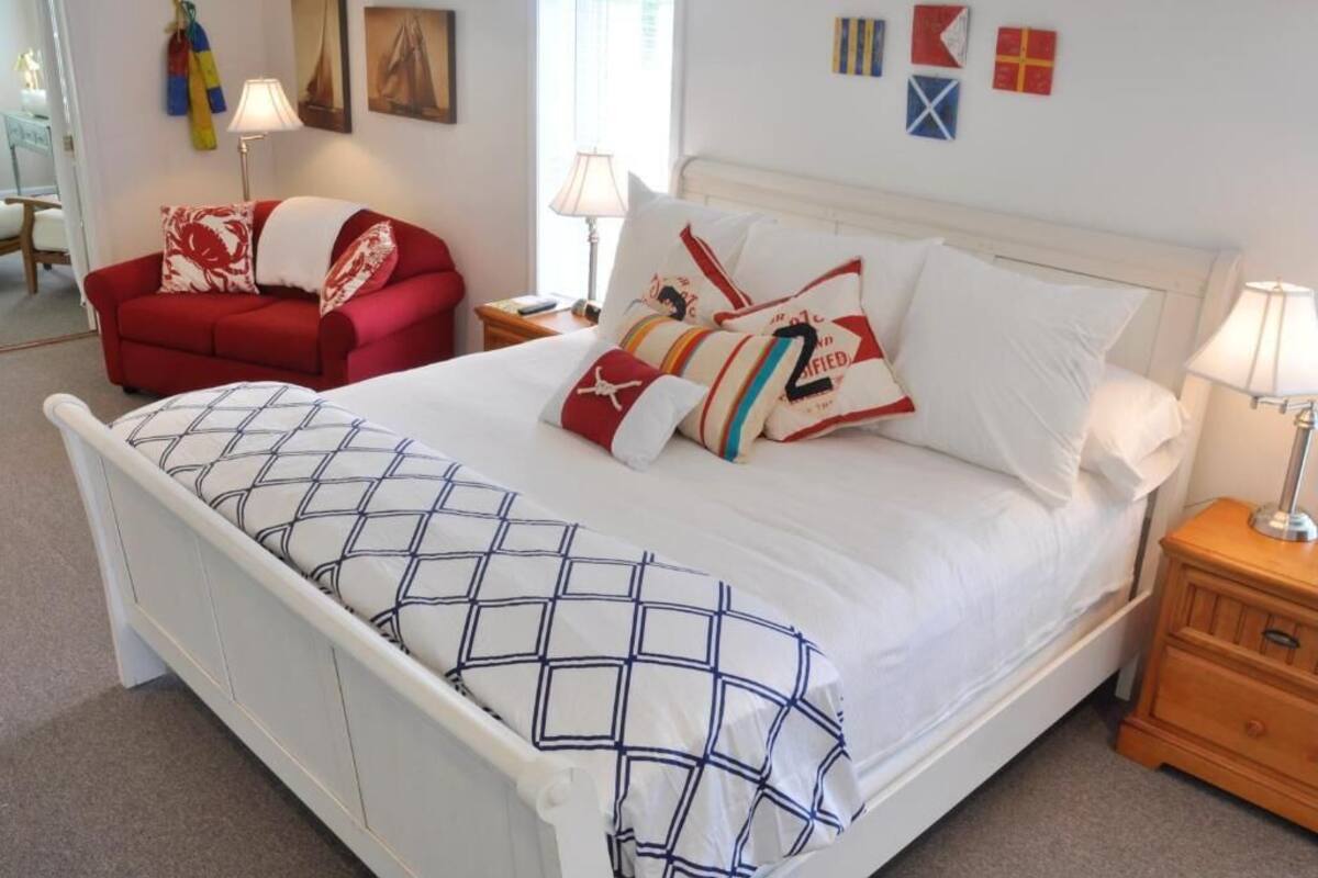 Un dormitorio ordenado con una cama, un sofá rojo y una mesita de noche con una lámpara.
