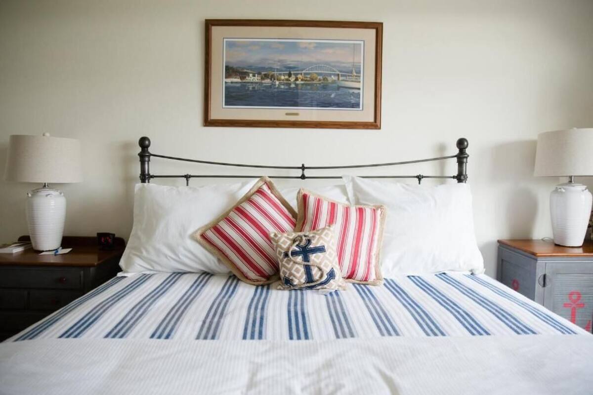 Una cama bien hecha con ropa de cama a rayas y almohadas decorativas, un cuadro en la pared y lámparas de noche a ambos lados.