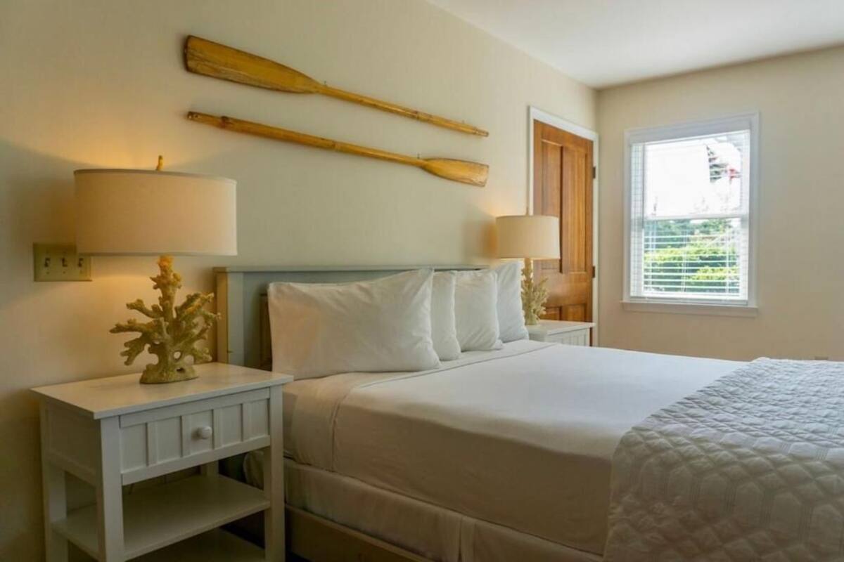 Un dormitorio con una cama, dos mesitas de noche, una lámpara, un adorno y una ventana con persianas.