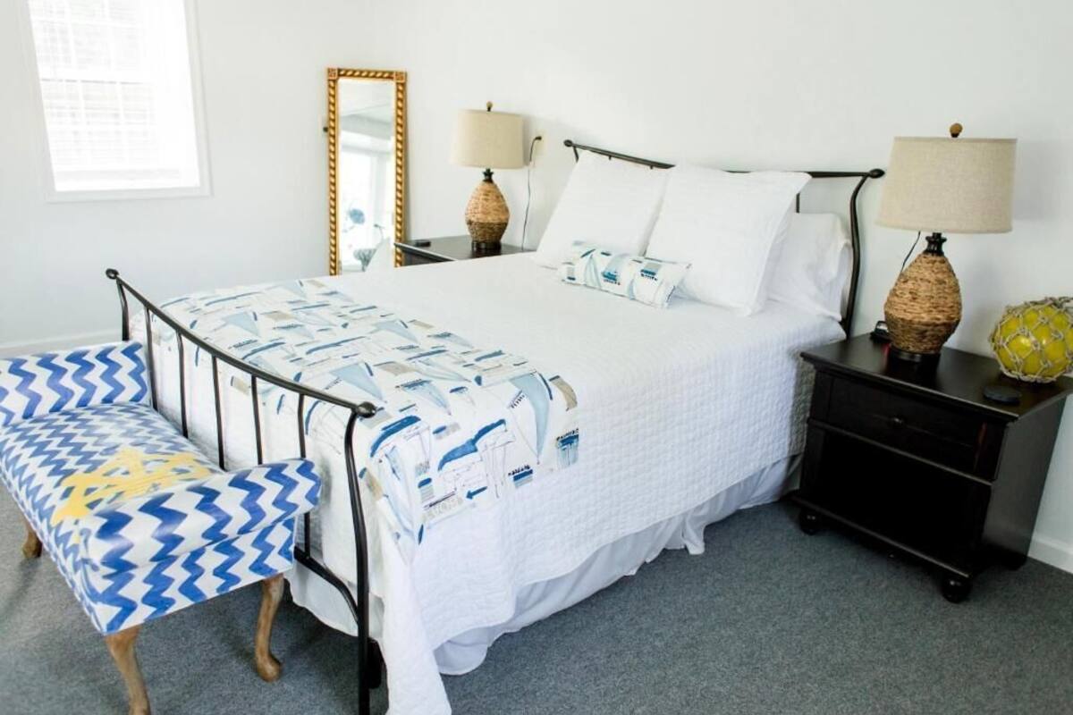 Un dormitorio ordenado con cama, mesitas de noche, un banco y un espejo.