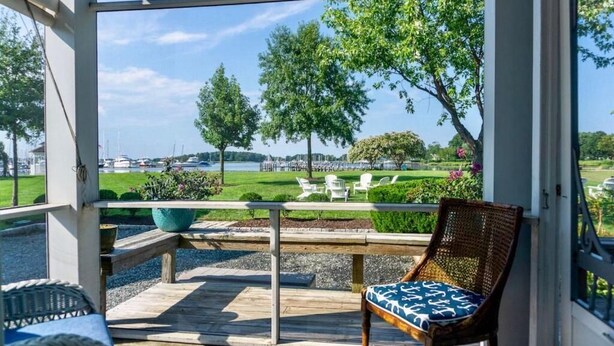 A covered outdoor seating area with a view of a landscaped garden and a body of water. - Inn at Haven Harbour (Rock Hall)