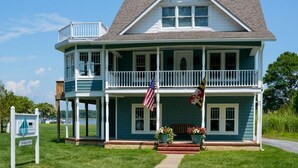 A two-story house with a balcony, a porch with potted plants, and a flag. - Inn at Haven Harbour (Rock Hall)