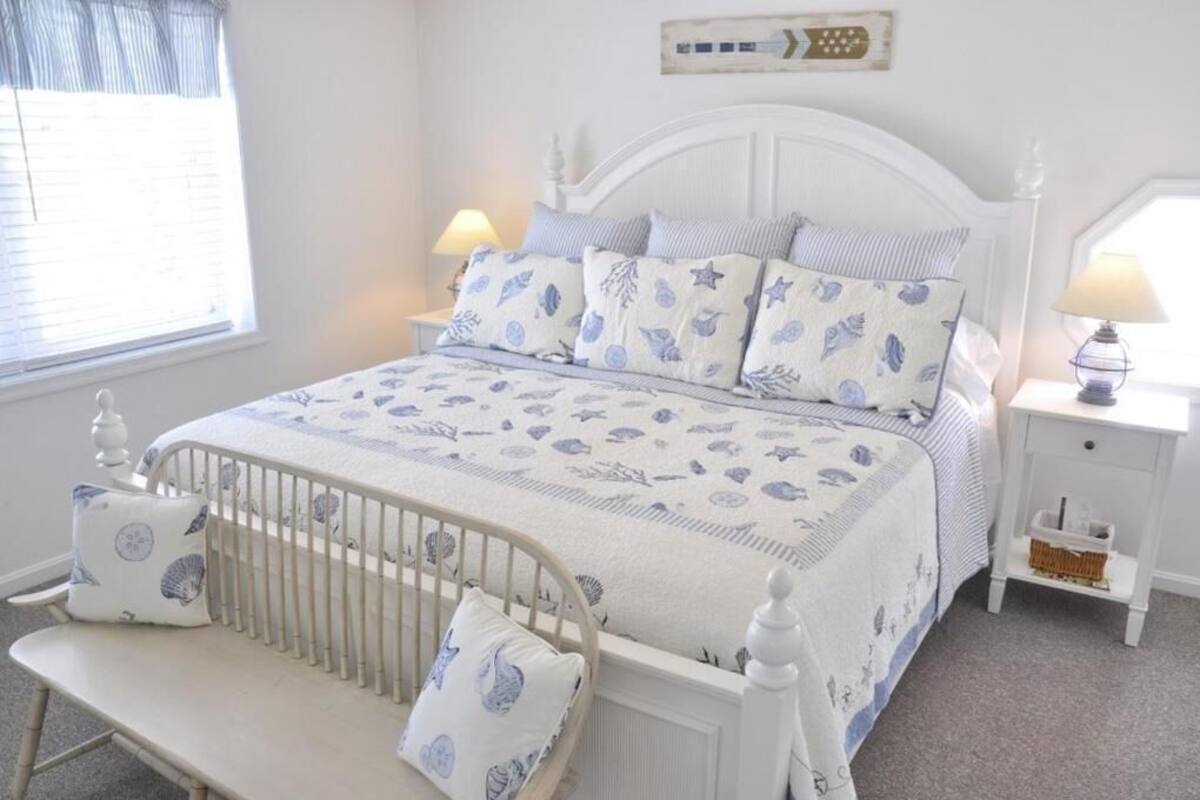 Un dormitorio ordenado con una cama blanca, mesitas de noche a juego y una cuna.
