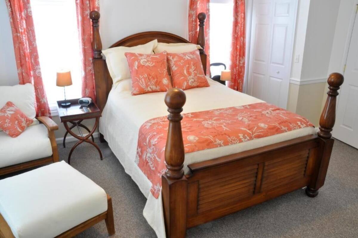 Un dormitorio ordenado con una cama de madera con dosel, una mesita de noche con lámpara y una silla.