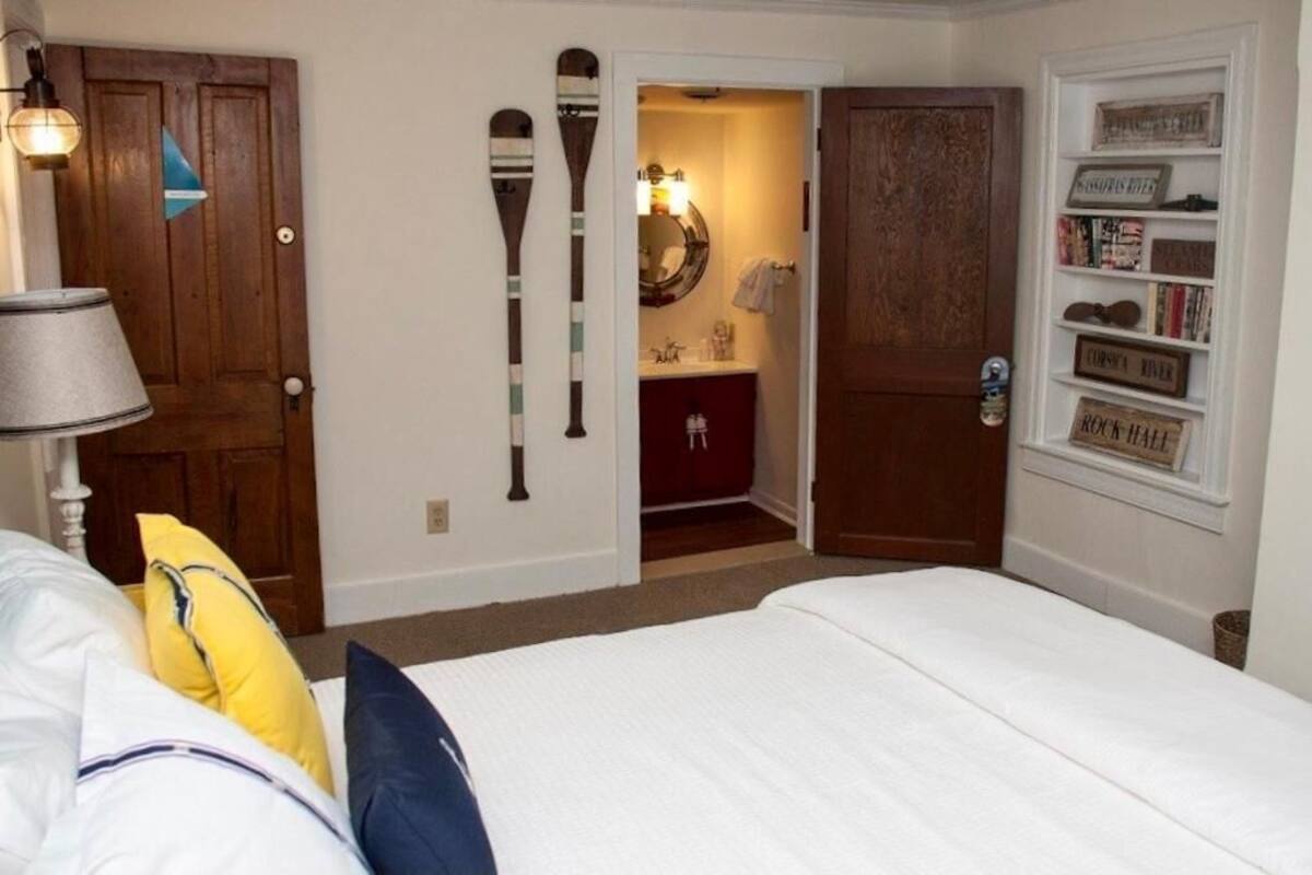 Un dormitorio con cama, mesita de noche, lámpara, armario y puerta que da a un baño.
