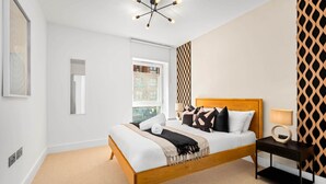 Une chambre moderne avec un lit en bois, une table de chevet, une lampe fixée au mur et un mur orné d’un motif.
