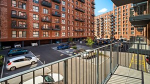 Un immeuble résidentiel à plusieurs étages, doté d’une façade en briques, de balcons et d’un espace de stationnement où sont garées des voitures.
