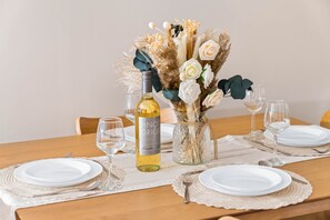 Ein Esstisch, gedeckt mit weißen Tellern, einer Flasche Pinot Grigio und einer Vase mit Blumen und Pampasgras.