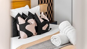 Ein ordentlich bezogenes Bett mit schwarz-weiß gemusterten Kissen, einem aufgerollten weißen Handtuch und einem hölzernen Kopfteil.