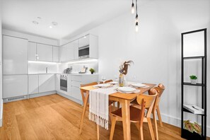 A modern kitchen with white cabinets, a wooden dining table set for four, and a black shelving unit with plants. - Luxury Apartment - Balcony - Fast WiFi - Netflix (Birmingham)