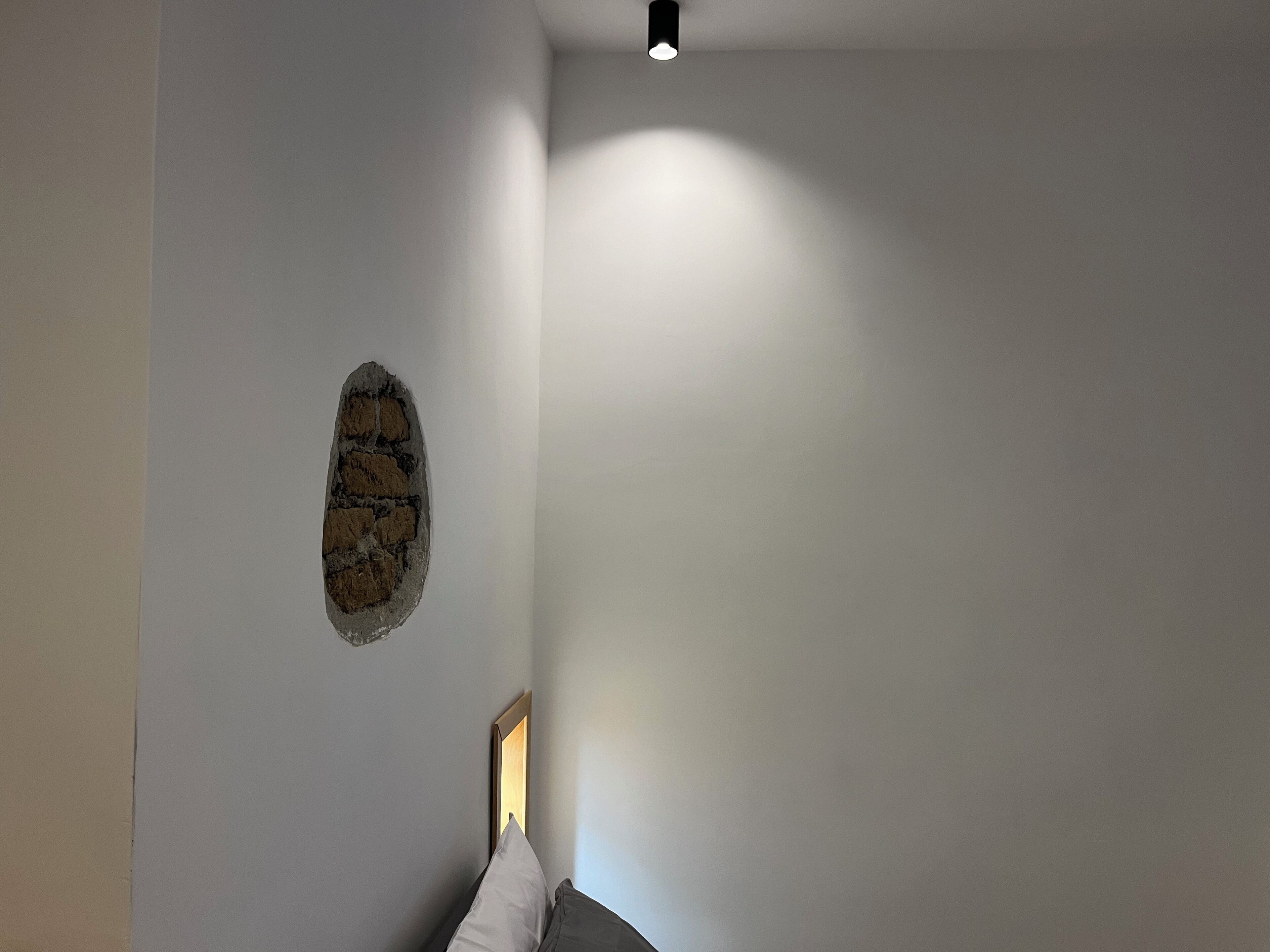 A room with a stone accent wall, a bed with a headboard, and a ceiling light.