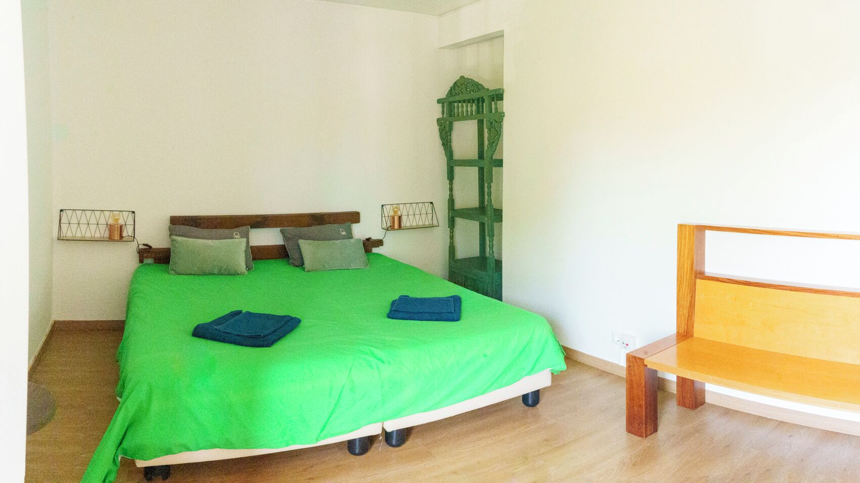 Een kamer met een bed, een bankje en een groene stoel.