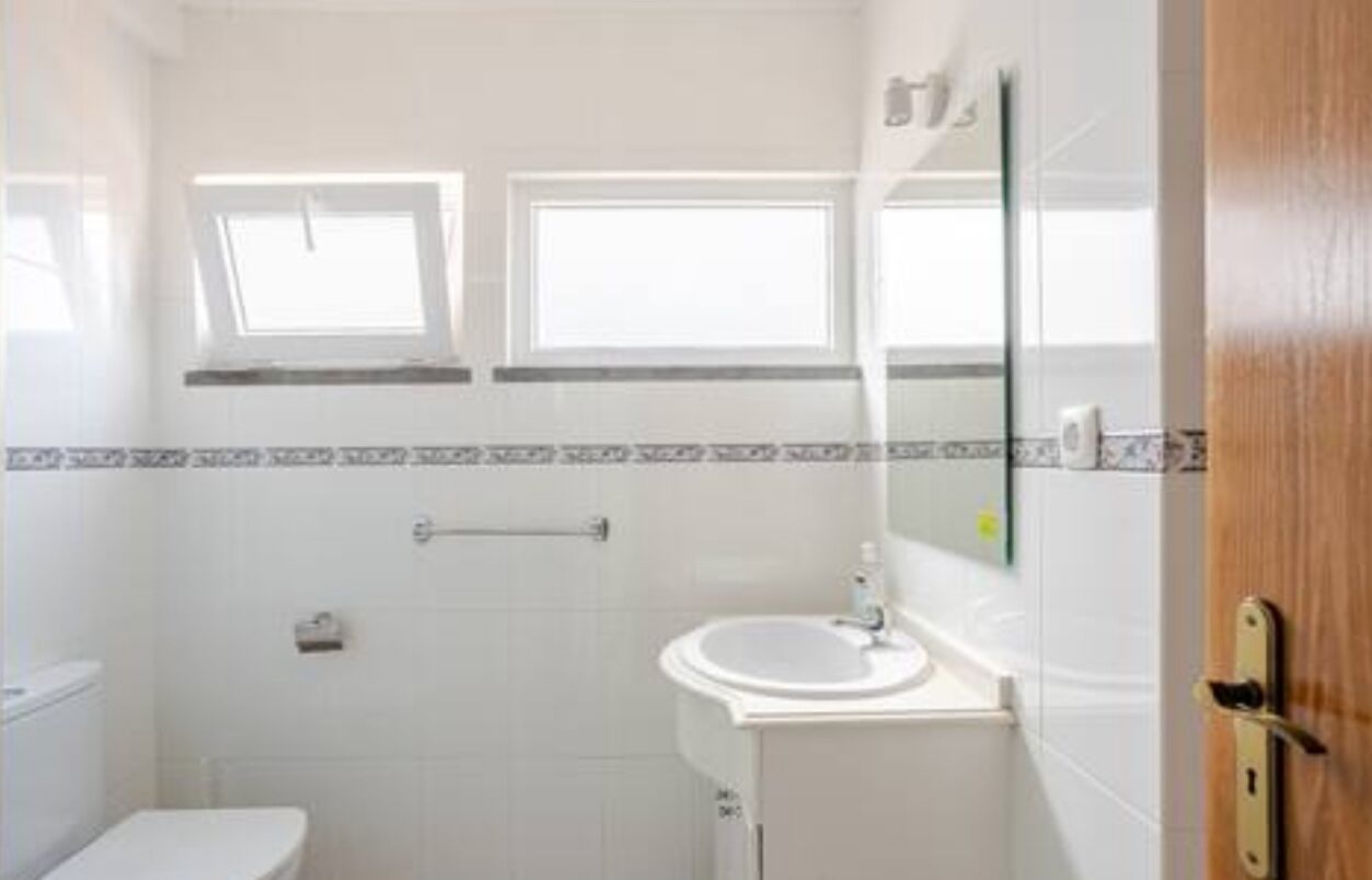 Ein kleines, sauberes Badezimmer mit Toilette, Waschbecken und zwei Fenstern.