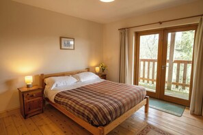 A bedroom with a wooden bed, two bedside lamps, a framed picture on the wall, and a view of the outdoors through a sliding glass door. - Owl's Roost Eco Lodge Apartment, Lampeter (Lampeter)