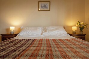 Ein Hotelzimmer mit einem großen Bett, zwei Nachttischlampen, einem gerahmten Kunstwerk an der Wand und einer Blumenkomposition auf dem Nachttisch.