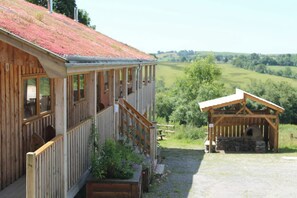 A wooden building with a balcony, a covered wooden structure, and a view of green fields.