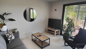 A modern living room with a grey sofa, a coffee table, a TV stand, and a large window with blinds.