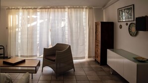 Un salon comprenant un fauteuil en osier, une table basse en bois, un canapé blanc, un meuble et un mur orné d’un tableau encadré et d’assiettes décoratives.