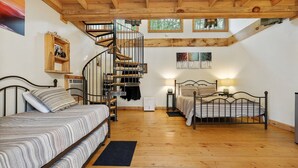 A bedroom with a wooden floor, a bed, a second bed, a spiral staircase, and a window with a view of trees. - Fairytale SQUIRREL'S NEST cabin at Mulberry Gap in Ellijay! (Ellijay)