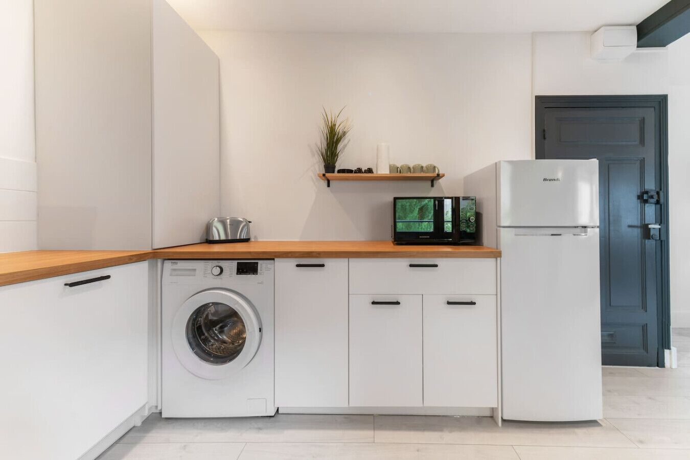 A compact kitchen with a washing machine, a microwave, and a refrigerator.