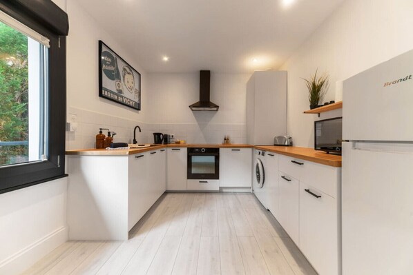 A modern kitchen with white cabinetry, a built-in oven, a microwave, and a washing machine.