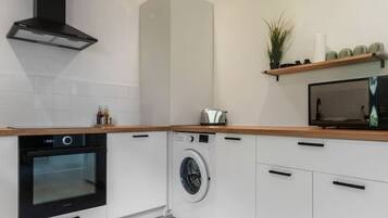 Een moderne keuken met witte kastjes, een inbouwoven, een wasmachine en een magnetron op een houten aanrecht.