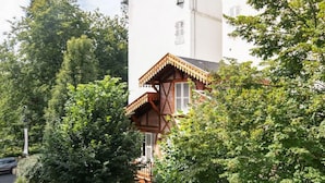 A two-story building with a white facade, a wooden balcony, and a green roof.