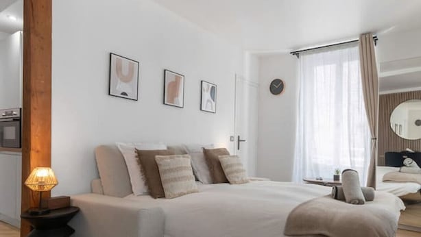 A modern bedroom with a large bed, a bedside table with a lamp, and a wooden beam structure.
