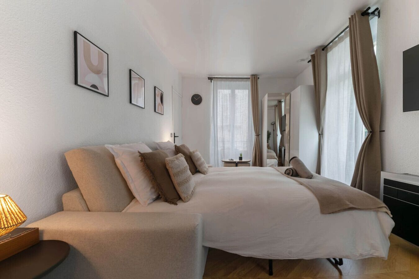 A modern bedroom with a large bed, a bedside table, a lamp, and a view of the bathroom through an open door.