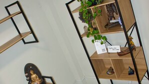 Un rincón de una habitación con un escritorio, una computadora portátil, una pequeña estatua de Buda, una planta y una estantería con objetos decorativos.