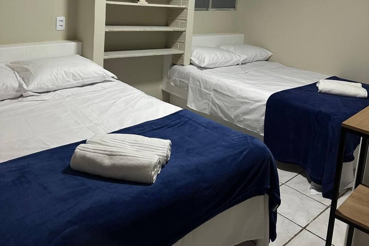 A hotel room with two beds, a wardrobe, a small table, and an air conditioning unit.