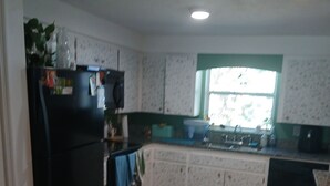 Eine Küche mit einem schwarzen Kühlschrank, weißen Schränken, einem Fenster mit grüner Einfassung und einem gefliesten Boden.