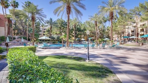 Zona de piscina en un resort, con palmeras, sillas de descanso y sombrillas.