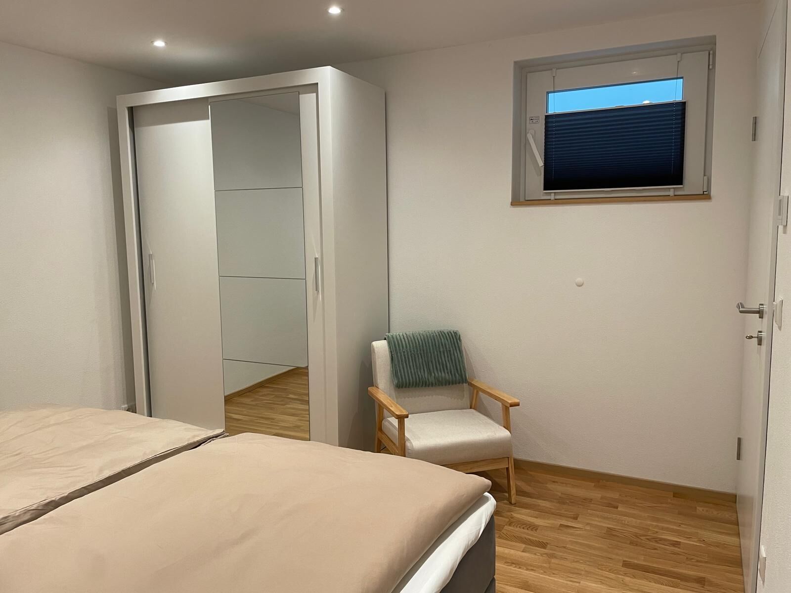 Une chambre à coucher avec un lit, une chaise, une armoire et une fenêtre avec des stores.