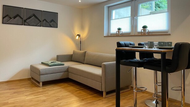 A modern living room with a sofa, a dining table with chairs, a floor lamp, and a window with blinds.