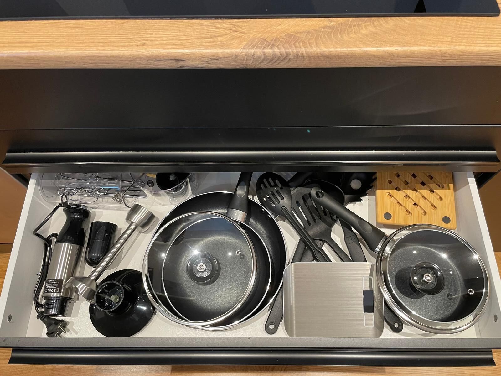 Uma gaveta de cozinha com diversos utensílios e eletrodomésticos, incluindo panelas, frigideiras e uma cafeteira.