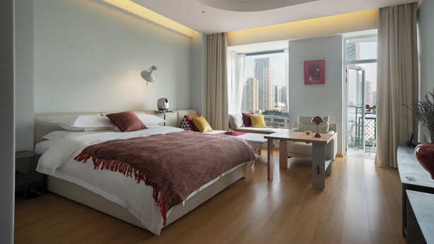 Una habitación de hotel moderna con una cama grande, un escritorio y un balcón con vistas a la ciudad.