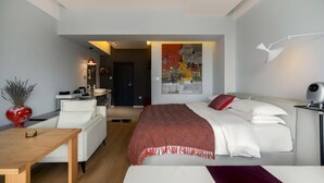 Una habitación de hotel moderna con una cama, un escritorio, una silla y un cuadro grande en la pared.