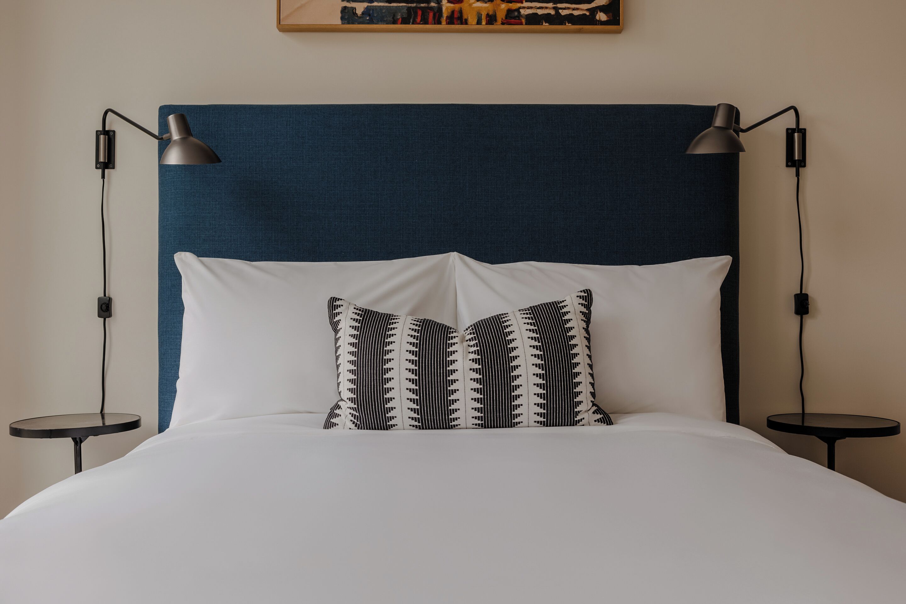 A neatly made bed with a blue headboard, two bedside lamps, and a patterned pillow.