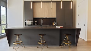 A modern kitchen with a central island, three stools, pendant lights, and wooden cabinets. - Sosuite at The Onyx - Museum District (Philadelphia)