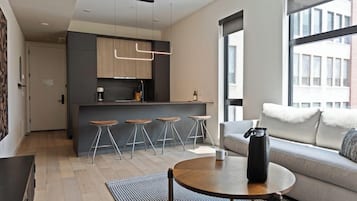 A modern living room with a sofa, a coffee table, and a kitchen area with bar stools.