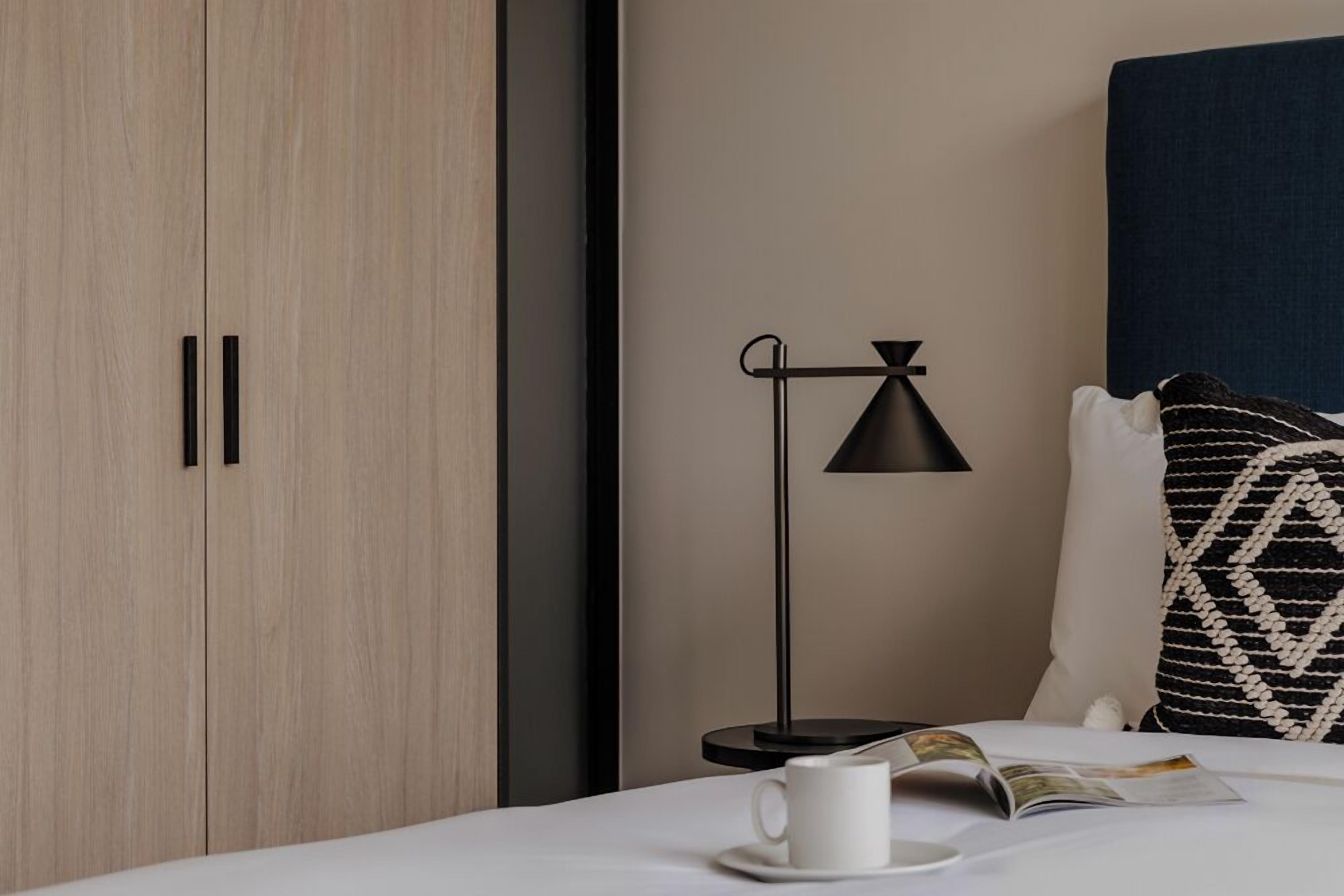 A neatly arranged bedroom with a bed, a bedside table with a lamp, and a wardrobe.